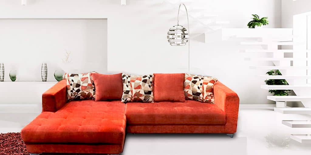 Se observa una sala esquinera tapizada en suede color rojo que destaca por su diseño moderno y acogedor. Los cojines decorativos con patrones geométricos complementan el conjunto.