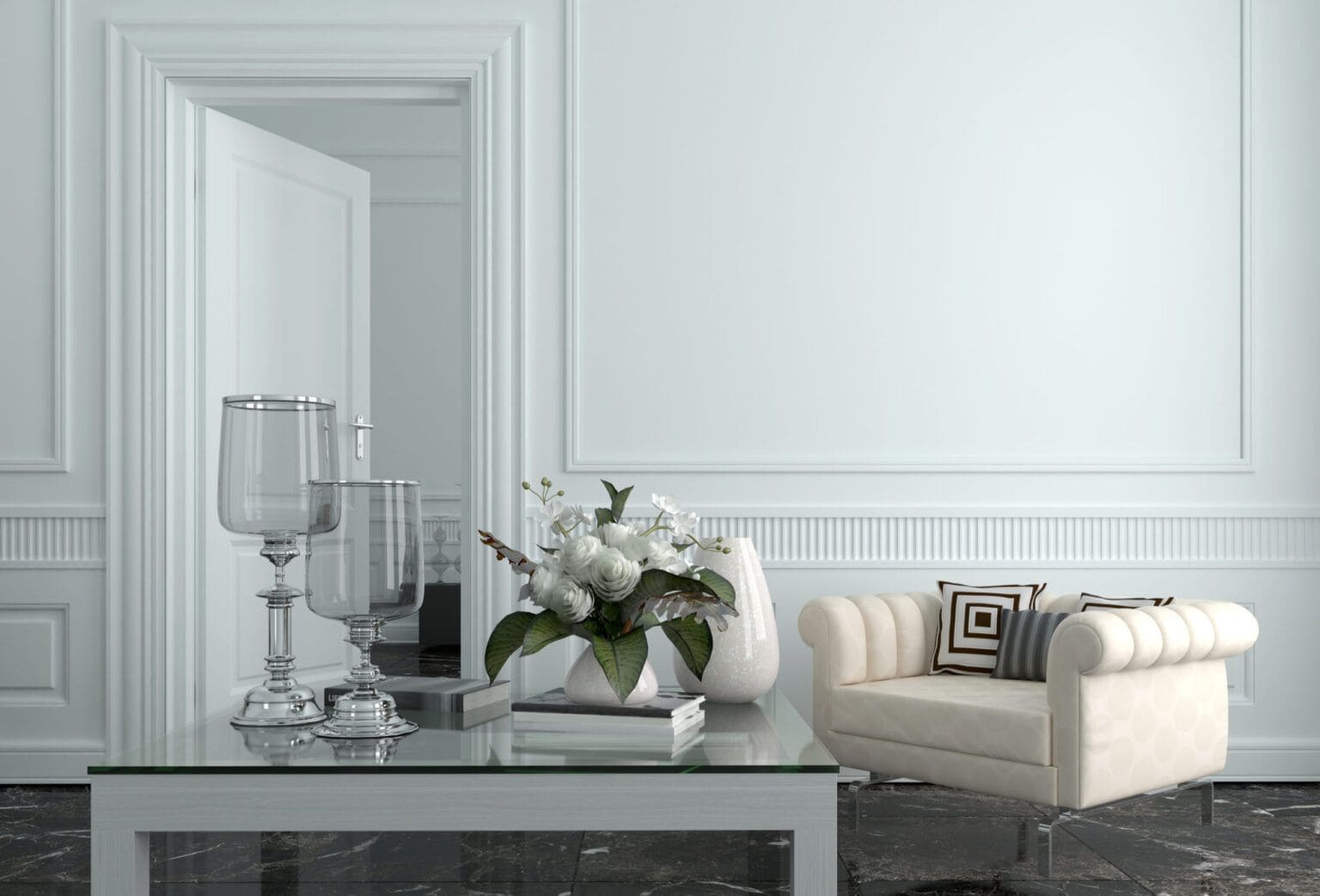 La imagen presenta una sala de estilo clásico con paredes blancas molduradas, un sofá capitonado en tono claro y una mesa de cristal decorada con floreros y arreglos florales. La composición transmite elegancia, amplitud y luminosidad.