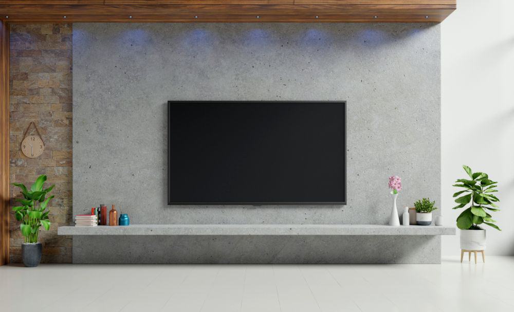 Se observa un espacio para televisión con diseño minimalista, donde destaca un panel de concreto acompañado por una repisa flotante del mismo acabado. La decoración con plantas y accesorios crea un ambiente limpio y equilibrado.