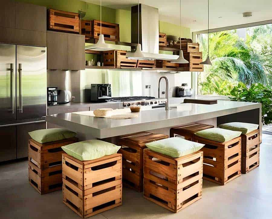 La imagen muestra una cocina de estilo natural y sostenible, donde se utilizan cajas de madera recicladas como bancos y elementos decorativos. La combinación de tonos madera, acabados modernos y abundante luz natural crea un ambiente creativo.