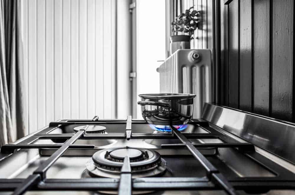 La imagen muestra una parrilla de gas con acabado en acero inoxidable y quemadores de alta resistencia. Se observa una olla sobre la flama encendida, resaltando un diseño funcional y moderno ideal para cocinas contemporáneas.