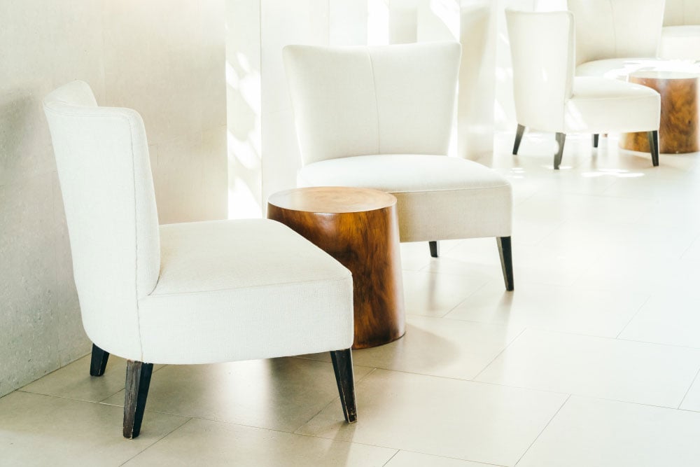 La fotografía muestra un conjunto de poltronas tapizadas en tono marfil con diseño minimalista y patas oscuras, ideales para crear una sala de espera elegante o un rincón de descanso. La mesa auxiliar de madera aporta un contraste cálido y moderno.