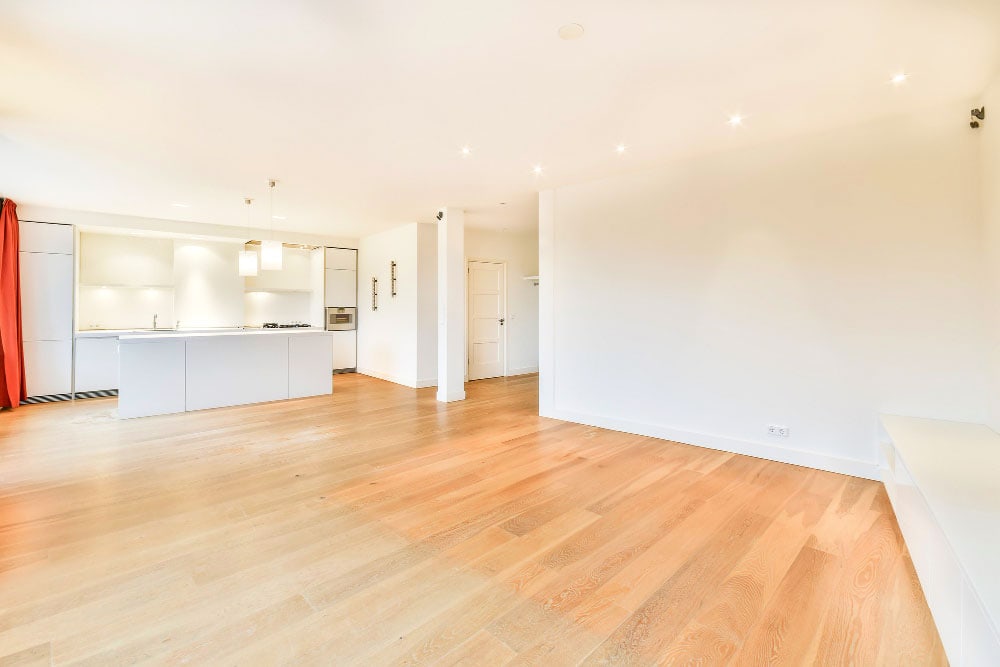 La imagen muestra un espacio amplio con cocina abierta y paredes en tonos claros, ideal para personalizar con fotografías o cuadros decorativos. La iluminación cálida y el piso de madera crean un ambiente moderno, elegante y acogedor.