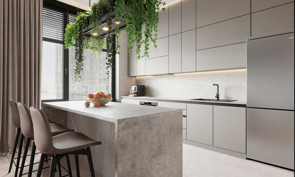 Una isla de cocina en acabado tipo concreto se convierte en el centro visual del espacio, combinando diseño minimalista, iluminación cálida y detalles naturales que aportan elegancia, amplitud y un ambiente moderno y sofisticado.