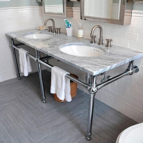 Un elegante mueble para baño con cubierta de mármol, doble lavabo y estructura metálica de acabado brillante. El diseño combina funcionalidad y estilo contemporáneo, mientras las toallas y los accesorios complementan un ambiente limpio.