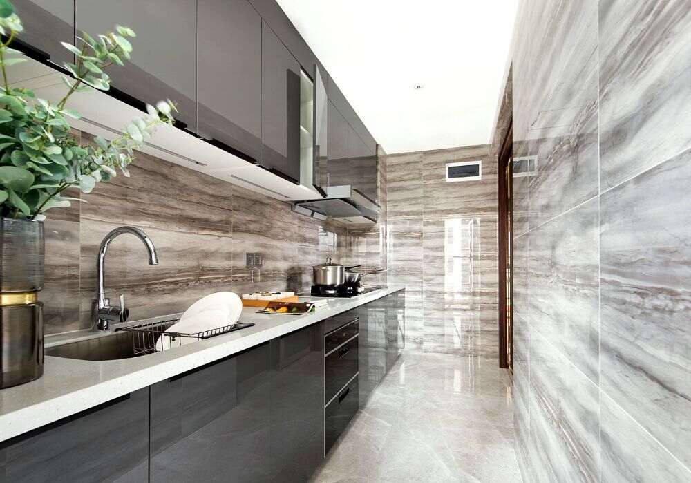 La imagen muestra una cocina contemporánea con gabinetes gris grafito de acabado brillante, cubierta blanca y revestimientos tipo mármol en tonos grises que aportan elegancia, amplitud y sofisticación.