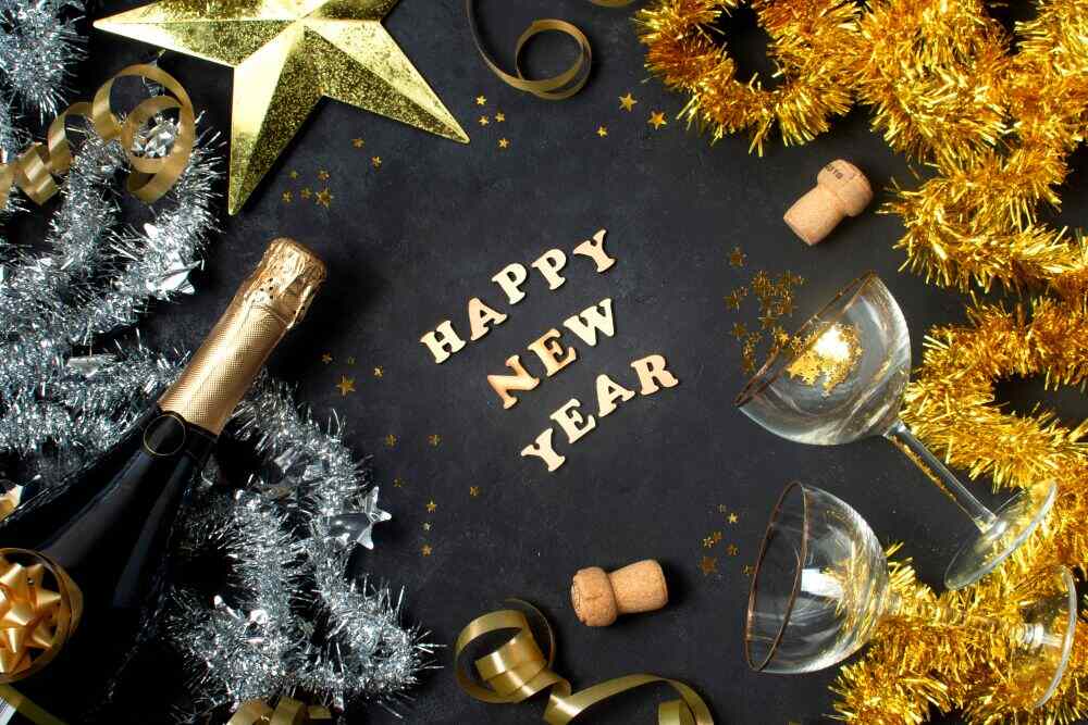 Se observa una composición festiva con copas, una botella de vino espumoso, serpentinas y adornos dorados y plateados, ideal para celebrar la llegada del nuevo año.