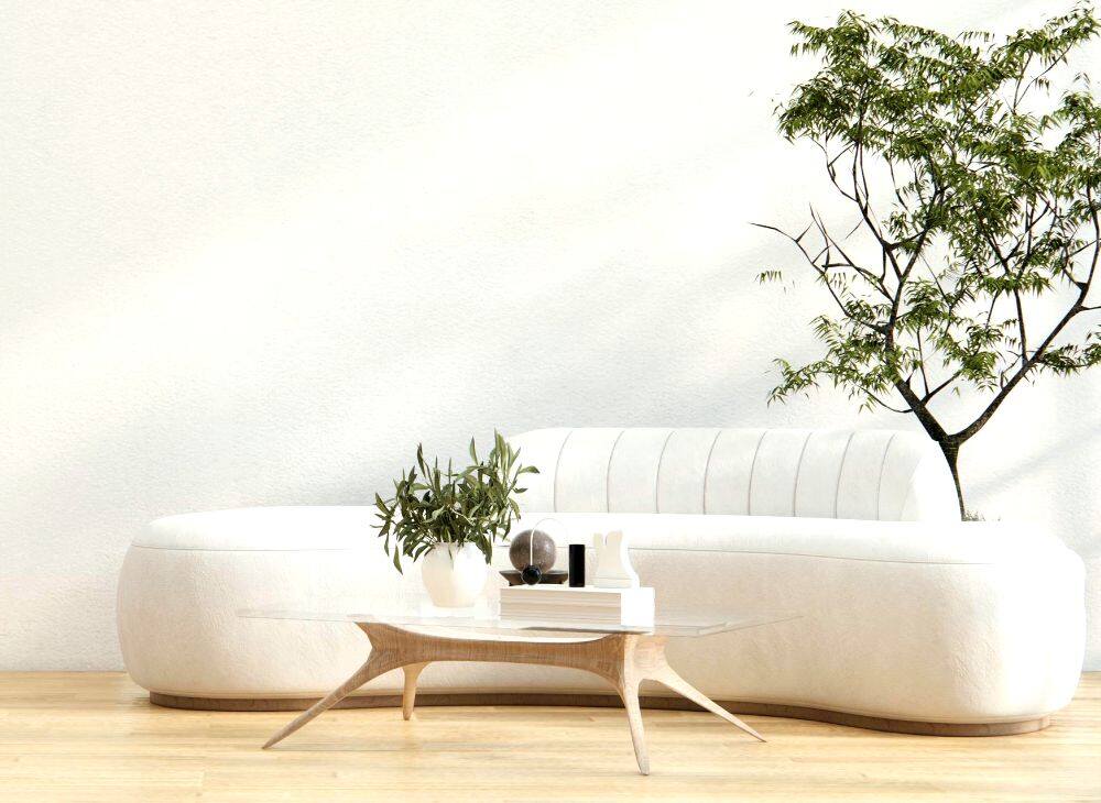 Se muestra una sala de estilo contemporáneo con un sofá curvo en color marfil y una mesa de centro de madera clara con cubierta de cristal. La decoración incorpora plantas naturales y una paleta de colores neutros que aporta elegancia.