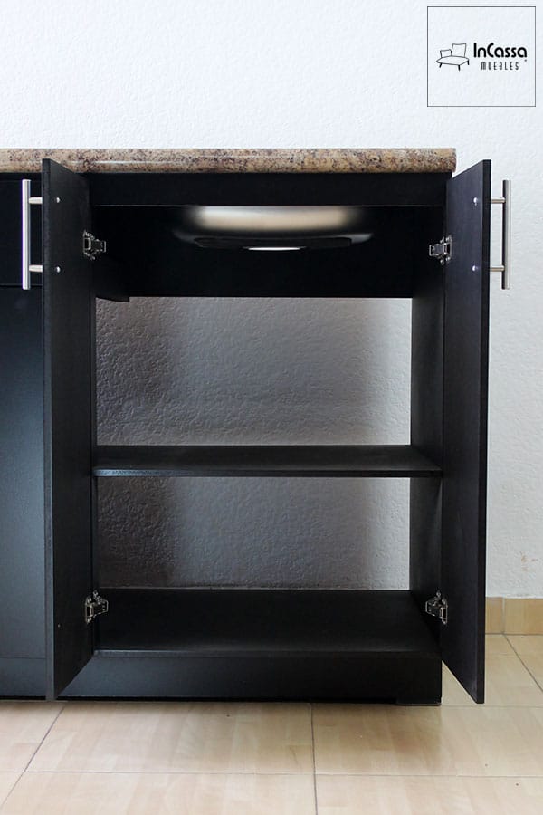 Detalle del módulo inferior chocolate en su sección derecha con ambas puertas abiertas, mostrando su interior dividido por una repisa y la parte inferior de la tarja de acero inoxidable instalada en la cubierta de formaica estilo piedra salvaje.