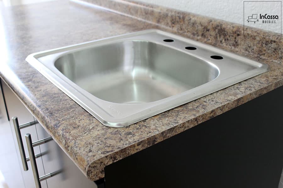 Primer plano que resalta la tarja de acero inoxidable empotrada en la cubierta de formica tipo piedra salvaje. El diseño práctico y moderno combina funcionalidad y estilo, ideal para optimizar el área de trabajo en cocinas compactas.