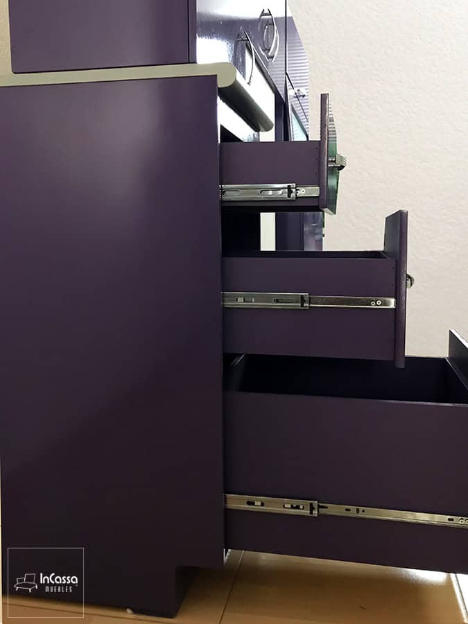 Una toma lateral del mueble carnicero de la cocina, en la que se muestra con sus tres cajones abiertos, estos son de color morado en su totalidad al igual que el resto del módulo, además de que cuentan con rieles metálicos para su apertura y cierre.