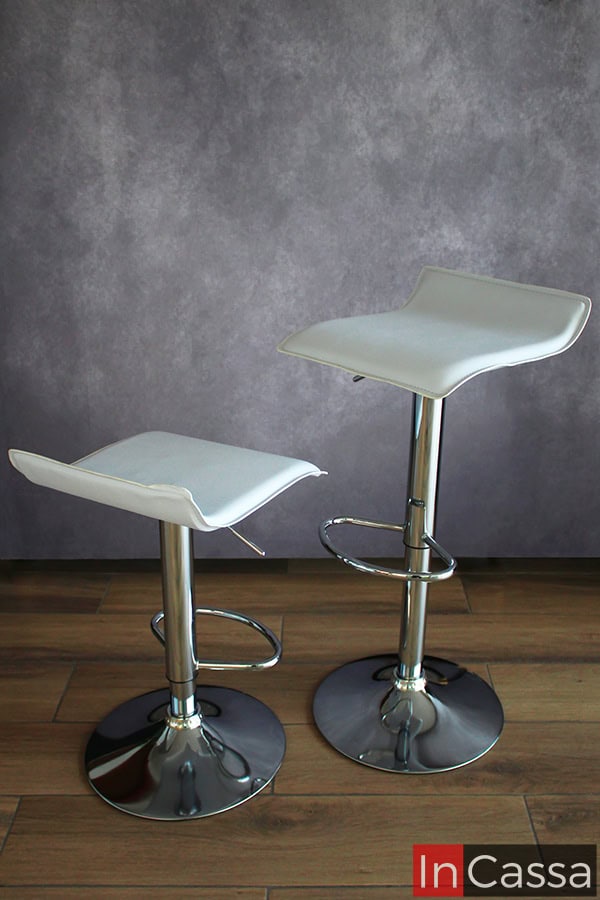 La imagen muestra los dos bancos altos incluidos en la cantina, los cuales cuentan con asientos blancos y una base metálica ajustable con reposapies. Cada banco es presentado con una altura distinta, a fin de mostrar su altura mínima y máxima.