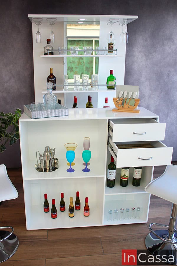 Esta toma frontal destaca los compartimentos que pueden encontrarse en la parta trasera de la barra incluida en la cantina. los cuales están divididos por entrepaños que conservan el tono blanco que puede observarse en el resto de la cantina. En esta sesión también pueden apreciarse dos cajones con jaladeras de arco y rieles metálicos para su apertura y cierre.