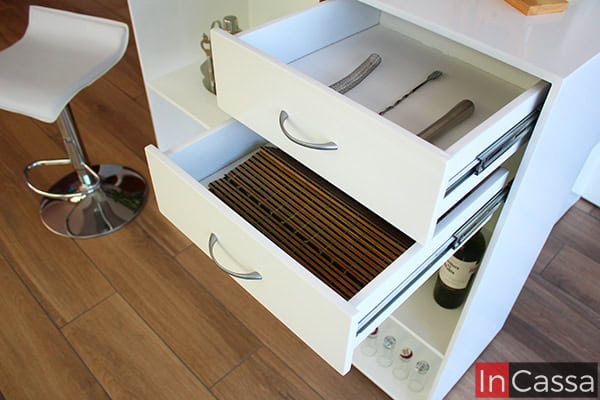 Una imagen de la barra incluida en la cantina con sus dos cajones abiertos. Estos son bastante amplios y cuentan con jaladeras metálicas con forma de arco, además de un sistema de rieles metálicos para su apertura y cierre. Cada uno de los cajones conserva el color blanco en la totalidad de su estructura, al igual que el resto de la barra.