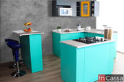 Una toma amplia desde el frente muestra la Cocina Modelo Aruba en forma de escuadra. El contraste entre los módulos inferiores turquesa, los superiores en gris medio con acento amarillo cromo y las cubiertas de formaica tipo mármol escalona da un estilo moderno y vibrante.