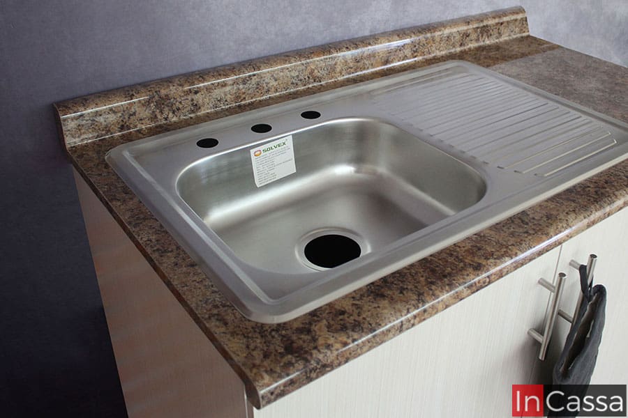 Esta toma se concentra en la tarja de acero inoxidable incluida en la cocina; siendo está una tarja de tina sencilla con escurridor. La foto además da una vista más cercana de la cubierta de formaica cuarzo café del módulo así como del acabado paja de este.