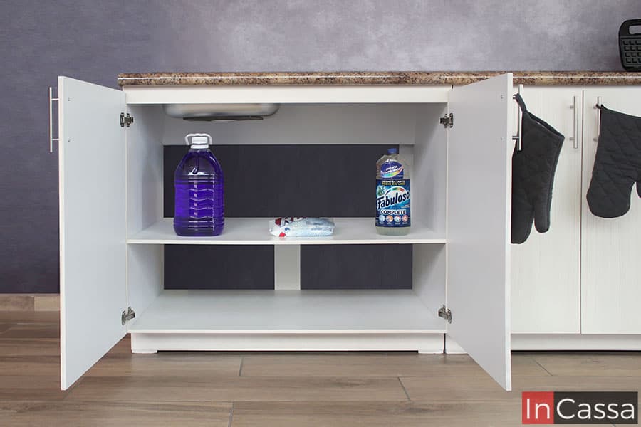 La toma se enfoca en el módulo inferior largo de la cocina, destacando la sección de tarja mostrándola con sus puertas abiertas dejando a la vista sus compartimentos interiores, estando estos divididos por un entrepaño horizontal. Cada una de las partes interiores del módulo son de color blanco.