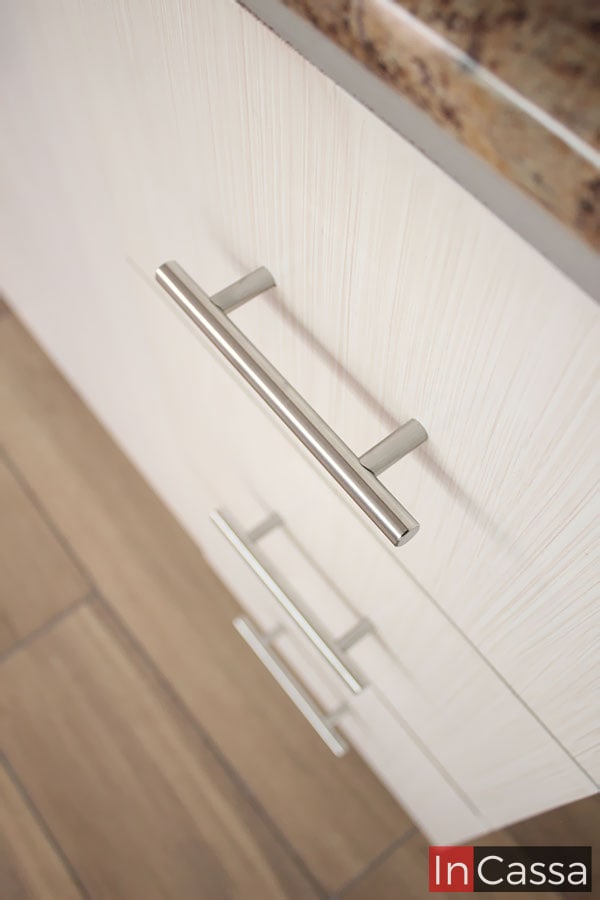 Una toma concentrada principalmente en mostrar de manera más detalla las jaladeras de los cajones, estas son metálicas en estilo de barra T, mismas que también se incluyen en las puertas de todos los módulos. La foto también permite apreciar de manera más cercana el acabado paja en la pintura del módulo.