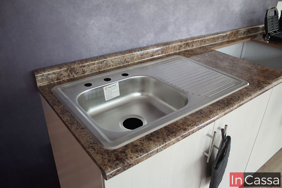 Foto de la tarja de acero inoxidable incluida en la cocina, la cuál cuenta con una tina sencilla y escurridor; la toma también deja a la vista gran parte de la cubierta de formaica en acabado cuarzo café, en la que además puede verse el hueco hecho para la instalación de una parrilla empotrable.