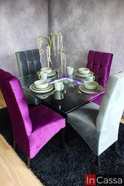 Moderno comedor diseñado para 4 personas, conformado por una mesa de cristal con arenero e iluminación LED, además de 4 sillas tapizadas con acabado capitoneado en color gris y morado. El comedor es presentado en una estancia con paredes grises y piso de madera.
