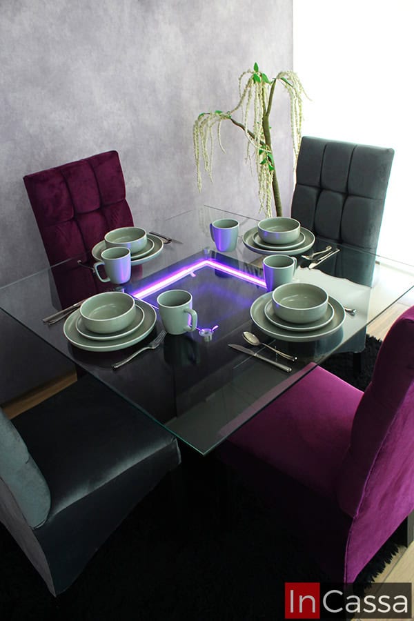 Foto del comedor completo, el cuál es visto desde una toma superior, destacando su mesa de cristal con iluminación LED y el acabado capitoneado en los respaldos de sus 4 sillas.