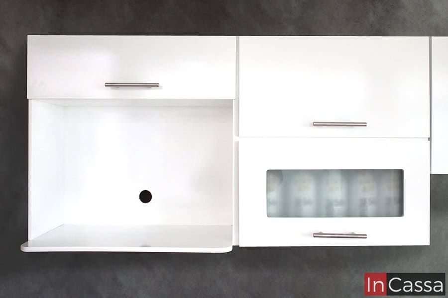 Alacena superior de la cocina con 3 compartimentos y un espacio para microondas. Las puertas de los compartimentos cuentan con jaladeras de barra T, y la estructura entera del módulo es de color blanco brillante.