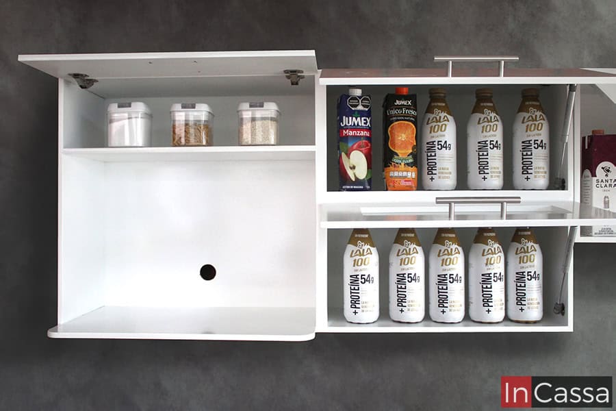 La imagen presenta el módulo porta microondas superior con sus tres puertas abiertas, estás cuentan con pistones neumáticos que permiten la apertura y cierre vertical de cada puerta. El módulo es exhibido con varios artículos en sus compartimentos a fin de ejemplificar su capacidad, además de que puede verse que sus interiores mantienen el mismo tono blanco que sus partes exteriores.