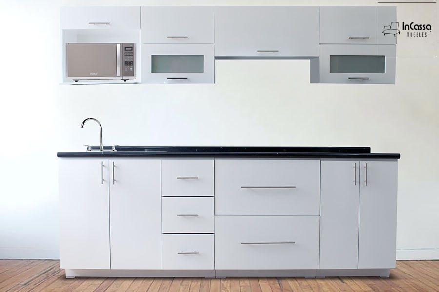 Una toma frontal que muestra la cocina integral modelo AUSTRIA completamente ensamblada. El mueble luce un elegante acabado en color blanco brillante, con cubierta de formaica estilo mármol negro que aporta contraste y modernidad. El diseño incluye espacio para microondas, campana, tarja, y una combinación funcional de puertas, cajones y vitrinas superiores con vidrio esmerilado. Ideal para cocinas contemporáneas que buscan estilo y practicidad.