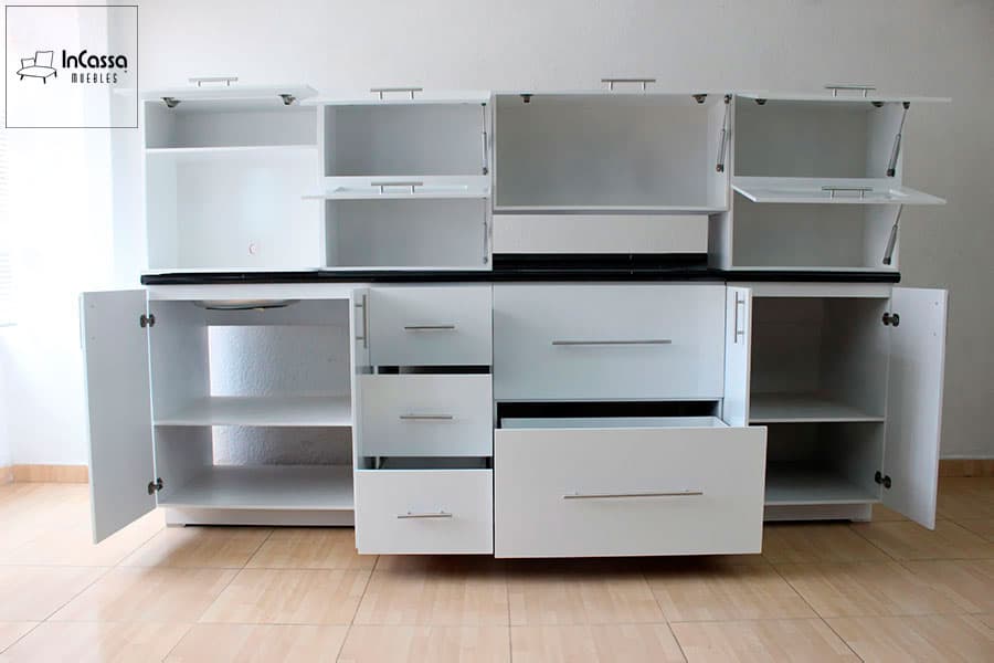 La imagen muestra la cocina modelo AUSTRIA con todas las puertas y cajones abiertos, revelando su funcional distribución interior. Fabricada en elegante color blanco brillante, incluye compartimentos superiores con pistones de gas, vitrinas de vidrio esmerilado y estantes internos. En la parte inferior, destaca la cubierta de formaica en estilo mármol negro y el amplio cajón central con correderas metálicas de extensión. Ideal para quienes buscan organización y estilo en un solo diseño.