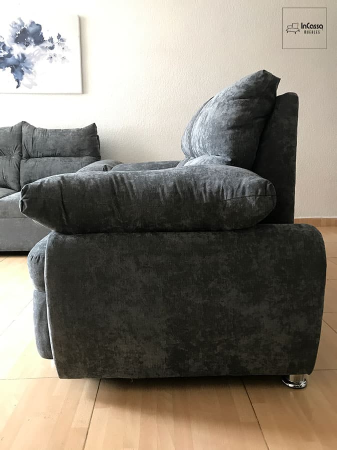 La foto presenta una vista lateral del love seat de la Sala Modelo Bora Bora, tapizado en suede gris oxford. Se distinguen los cojines de gran volumen en respaldo y brazo, que refuerzan la comodidad del diseño. El acabado aterciopelado del tapiz y las patas cromadas aportan un estilo elegante y contemporáneo al ambiente.