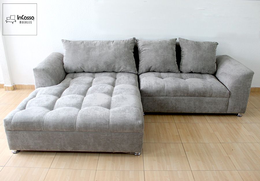 La Sala Esquinera modelo BANGLADÉS se muestra en una toma frontal completa, resaltando su tapizado en suede gris perla. Los asientos capitonados y cojines sueltos brindan gran comodidad, mientras que sus brazos rectos y patas metálicas aportan un estilo moderno y elegante.