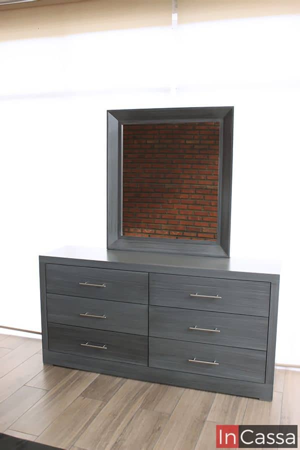 La foto presenta el tocador del modelo Barcelona en elegante tono gris cenizo oscuro, con sus seis cajones completamente cerrados y jaladeras metálicas. Se destaca su espejo cuadrado de marco robusto, ideal para complementar cualquier recámara moderna.