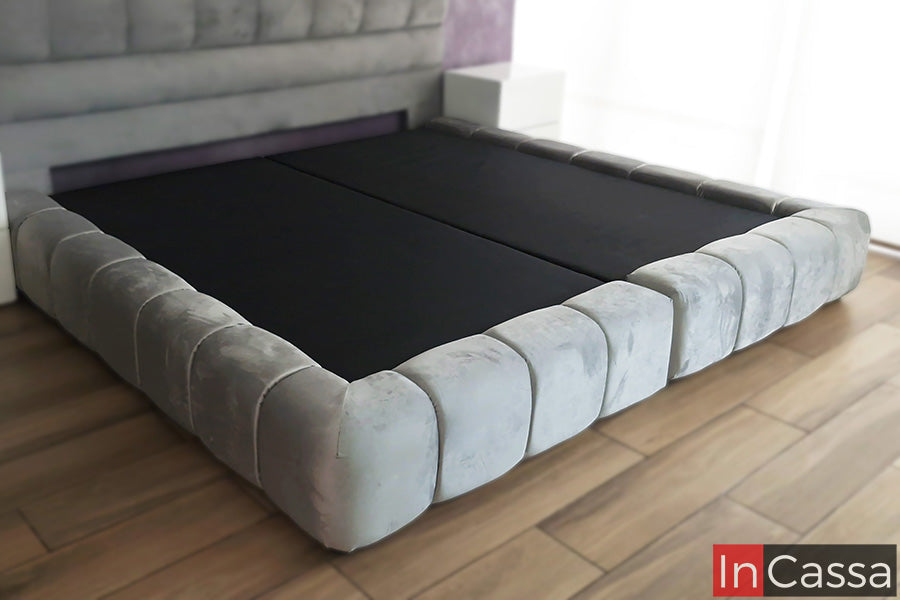 La imagen muestra la Base de Cama Tapizada Estilo Nube Modelo BURDEOS, tapizada en elegante suede gris perla. Su diseño acolchado con formas envolventes brinda una apariencia moderna y sofisticada, además de ofrecer una estructura resistente y confortable para complementar cualquier dormitorio.