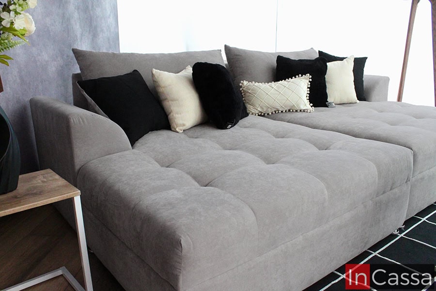 Esta vista cercana resalta el tapizado en suede gris perla suave y acolchonado de la sala, que ofrece gran comodidad. Los cojines negros y crema aportan contraste y estilo, añadiendo una sensación de calidez al espacio.