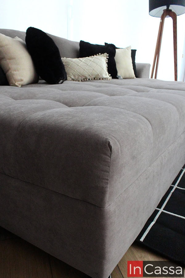 Esta imagen destaca la calidad del acolchado del sofá en tapiz suede gris perla, con un acabado que invita al confort. Las líneas limpias y los bordes redondeados refuerzan su diseño contemporáneo y funcional.