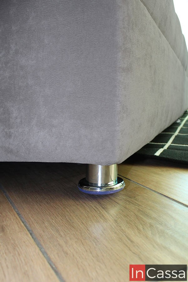 Un primer plano de la base del sofá muestra el tapizado suede liso en tono gris perla y las patas metálicas brillantes que elevan el diseño, manteniendo un equilibrio perfecto entre funcionalidad y estética.
