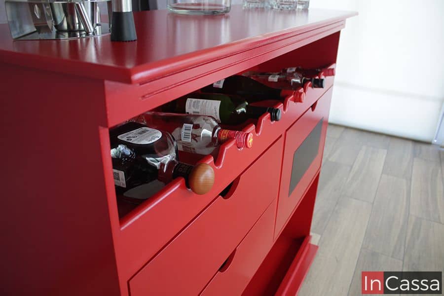 La foto presenta un ángulo lateral de la cantina Bonn en tono rojo vivo, resaltando la cava superior con diseño ondulado que mantiene las botellas seguras y a la vista. El acabado brillante y la superficie lisa realzan su estilo urbano y moderno.