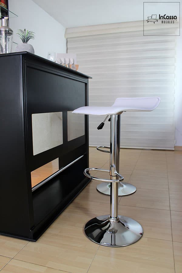 En esta toma lateral se aprecia la Cantina Bonn en color chocolate con cuadros decorativos blancos, junto al banco Urbino tapizado en blanco, destacando su base cromada con reposapiés y ajuste de altura. El contraste entre el tono oscuro de la cantina y el brillo metálico de los bancos realza un estilo moderno y elegante.