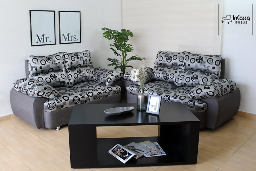 La imagen muestra la Sala Modelo Bora Bora en su versión tapizada en lino estilo geométrico gris con figuras circulares y cuadradas en tonos contrastantes. Incluye dos love seat con cojines acolchados que realzan la comodidad, complementados con mesa de centro negra y decoración moderna que aporta frescura y dinamismo al ambiente.
