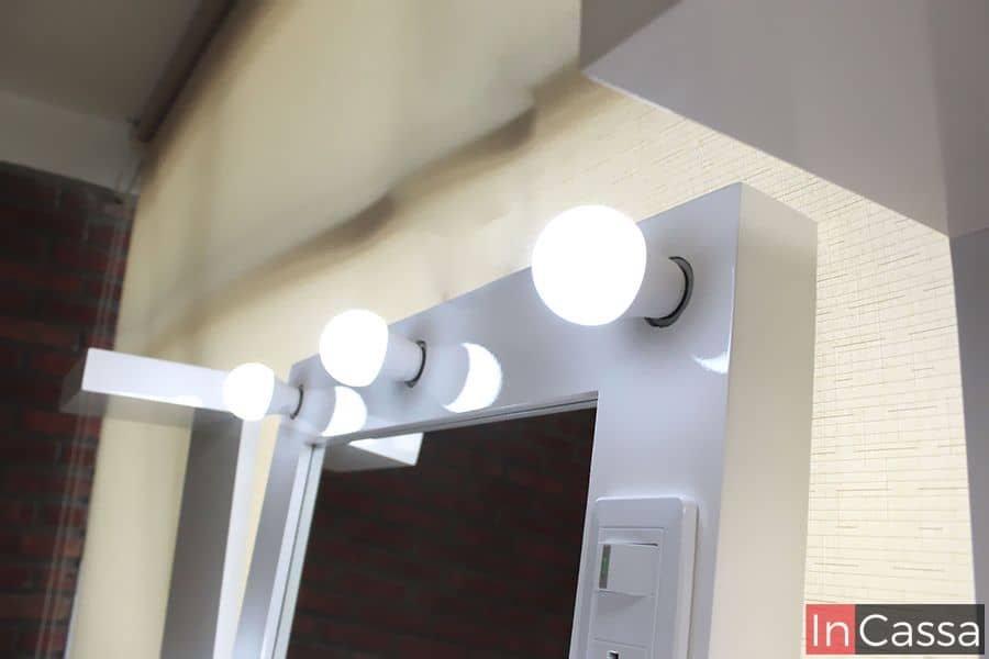 La foto presenta el detalle de las luces LED en el marco del espejo blanco, proporcionando una iluminación uniforme y moderna, perfecta para maquillaje y estilo.