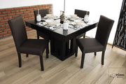 Una fotografía que presenta un comedor cuadrado para cuatro personas, compuesto por una mesa de líneas modernas en color chocolate y un pedestal central con diseño geométrico. Las sillas tapizadas en lino color chocolate complementan perfectamente el estilo contemporáneo del conjunto.
