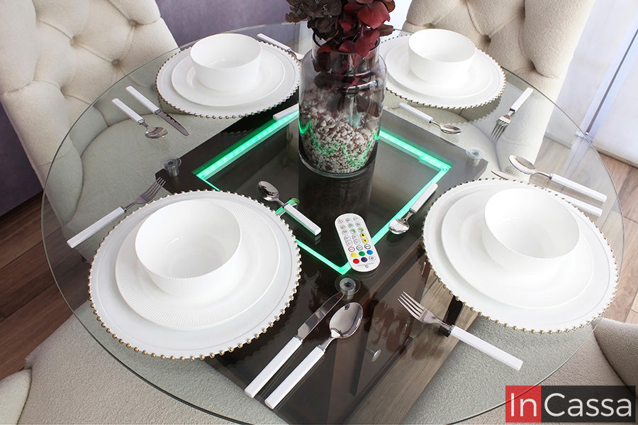 Se aprecia la mesa BRATISLAVA con cubierta de vidrio, destacando su iluminación LED integrada en el pedestal, que realza el centro decorativo y aporta un toque moderno y sofisticado al antecomedor.
