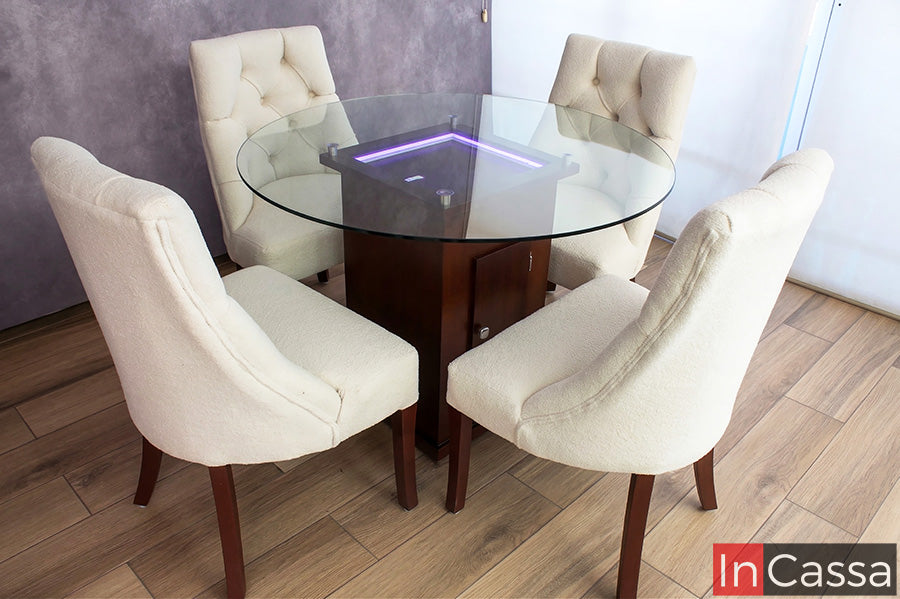 Se aprecia el antecomedor BRATISLAVA con mesa de vidrio y pedestal en color tabaco, resaltando su iluminación LED en tono violeta que aporta un ambiente moderno, acompañado de sillas capitoneadas en suede hueso.