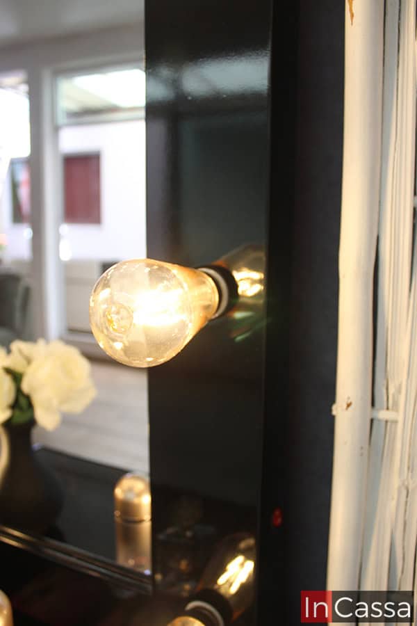 Imagen de uno de los nueve focos LED integrados al marco del espejo, ya que se muestra encendido podemos ver que es de luz cálida. Gracias al enfoque de la toma, es posible apreciar el acabado brillante en la pintura negra del marco.