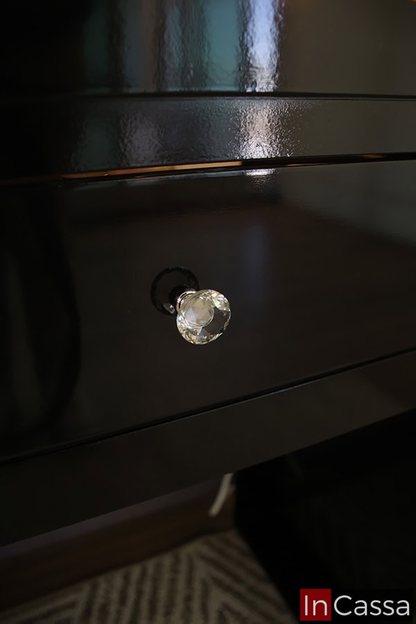 La toma se enfoca en la jaladera de estilo diamante integrada al cajón; por la cercanía de la foto, también queda resaltado el acabado brillante de la pintura negra del tocador.