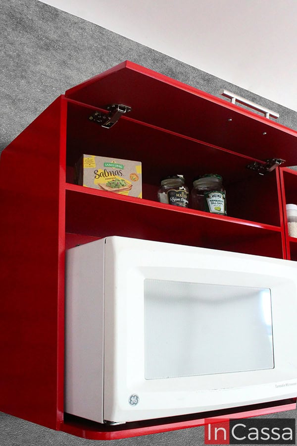 Esta foto resalta el módulo superior de la cocina integral roja completa, diseñado específicamente para incorporar un microondas. Encima, un compartimento con puerta abatible proporciona espacio adicional para almacenar alimentos no perecederos, manteniendo la organización y accesibilidad. Los herrajes metálicos garantizan durabilidad y un manejo fluido.