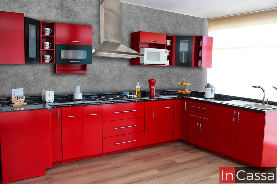 Una toma de la moderna cocina integral en U, diseñada en un vibrante tono rojo que resalta con cubierta de formaica estilo mármol negro. Sus múltiples módulos ofrecen almacenamiento amplio, mientras que los gabinetes superiores incluyen puertas de cristal esmerilado para un toque elegante. Esta cocina integra un diseño en U funcional, ideal para optimizar espacios, con áreas específicas para electrodomésticos como microondas y campana extractora. Un modelo que combina estilo y funcionalidad.