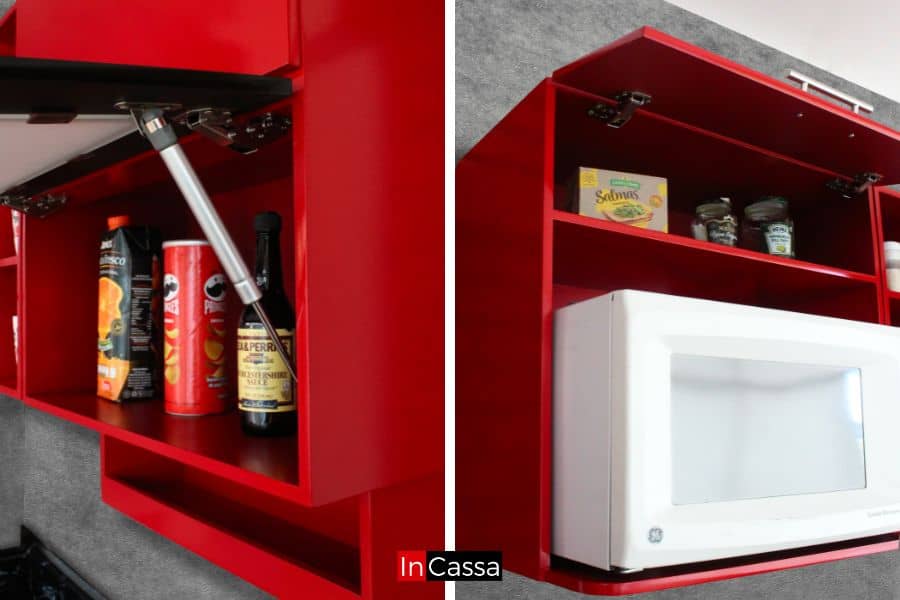 La foto muestra los gabinetes superiores de la cocina, resaltando los pistones neumáticos que garantizan una apertura suave y duradera. Diseñados para maximizar el almacenamiento, ofrecen compartimentos ideales para guardar alimentos y electrodomésticos como microondas, todo en un vibrante acabado rojo completo.