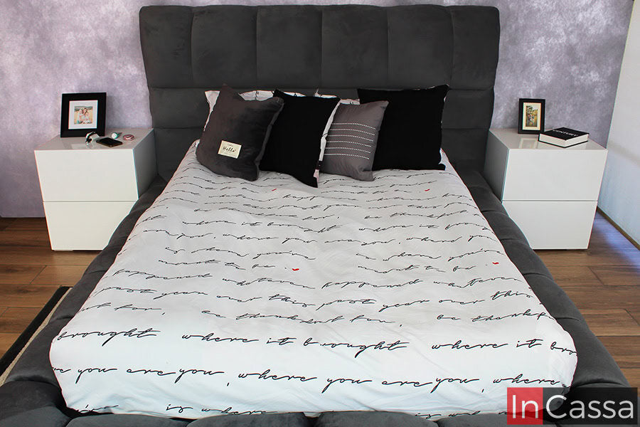 En esta toma se aprecia una vista directa de la cama, donde la cabecera y base tapizadas en suede gris oxford se convierten en el centro de atención, combinando a la perfección con la decoración moderna y los tonos neutros de las mesitas de noche.