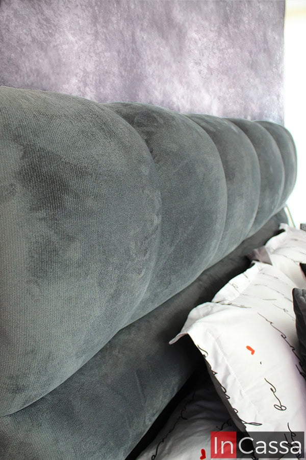 Este acercamiento de la cabecera muestra la textura suave del suede gris oxford y las costuras precisas que forman un patrón acolchonado tipo nube, resaltando el confort y el diseño exclusivo de esta pieza.